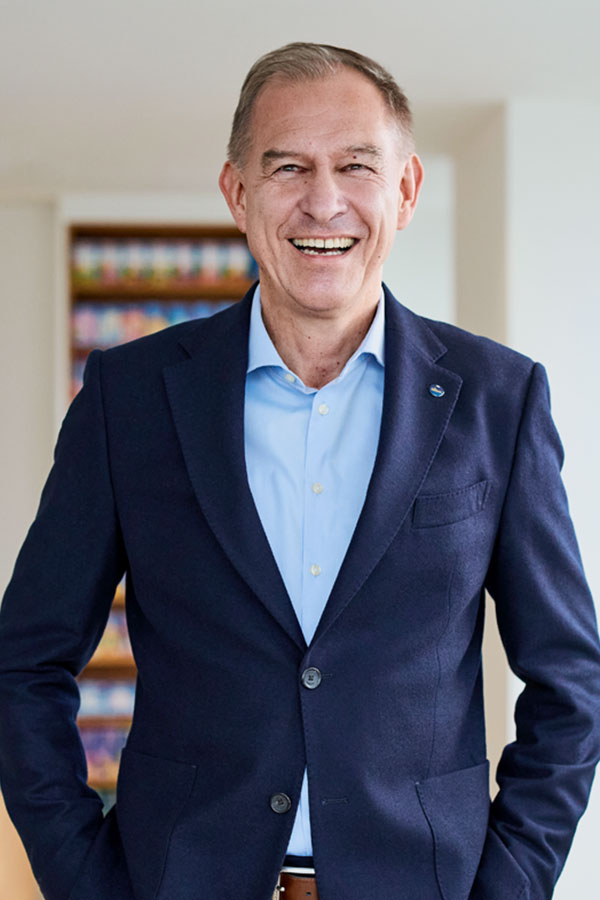 Portrait of Peter Amon, a board member of LSH. He has fair skin and short brown-gray hair. He is wearing a suit with a red tie and has his arms crossed while smiling. 